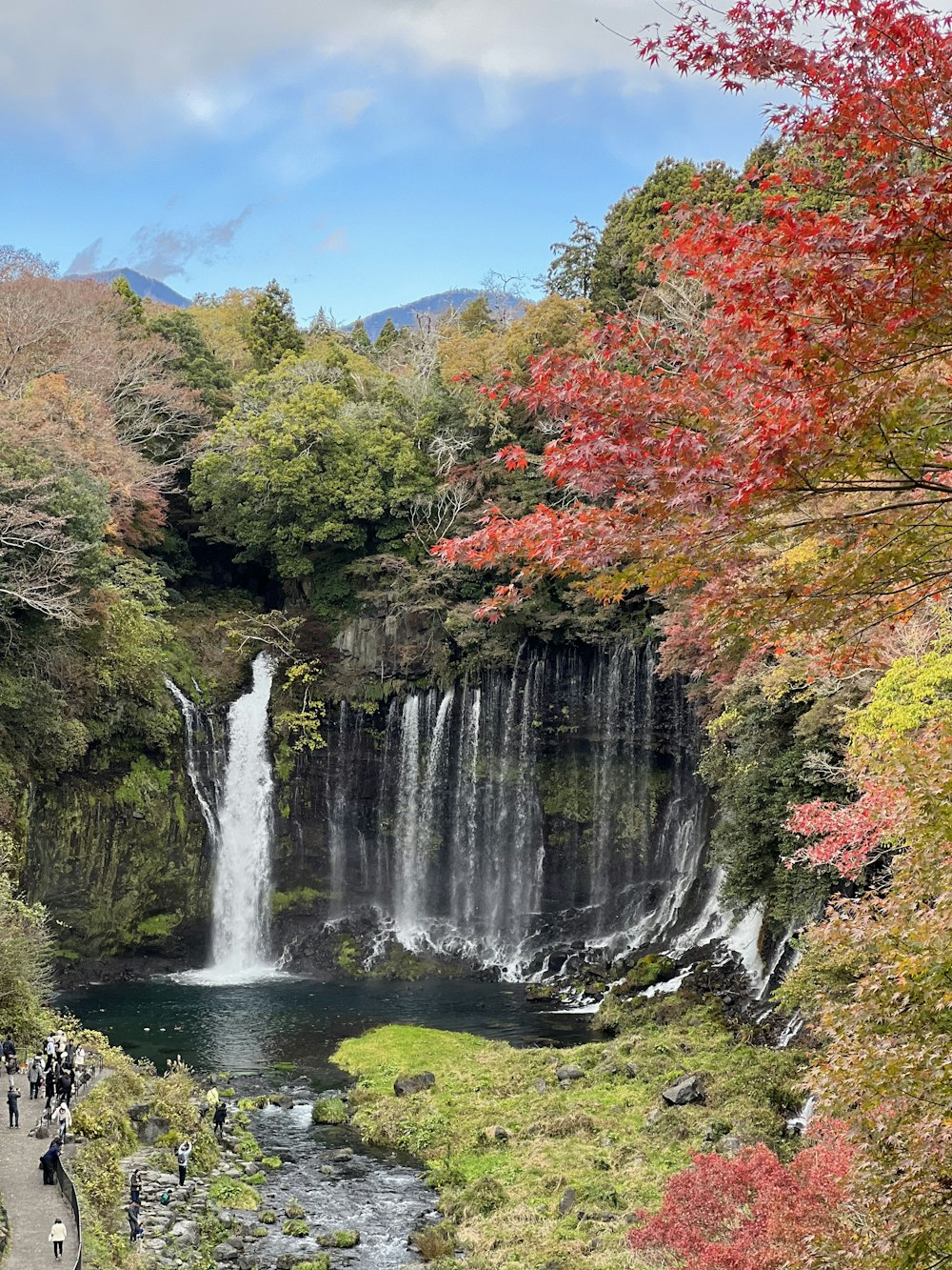 a waterfall surrounded by trees and people walking on a path