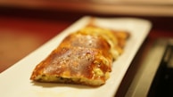A close-up view of several pieces of golden-brown baked pastry items arranged on a white rectangular plate. The pastries appear to be filled with a savory or cheesy filling, and the crust looks crispy and well-cooked.