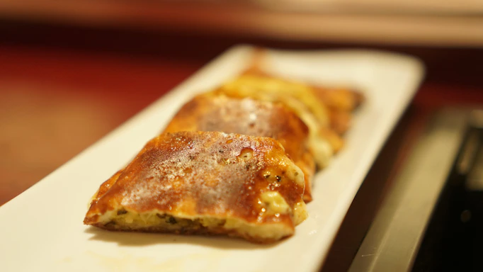 Close-up of a golden, crispy pastel filled with savory meat on a rustic wooden table.