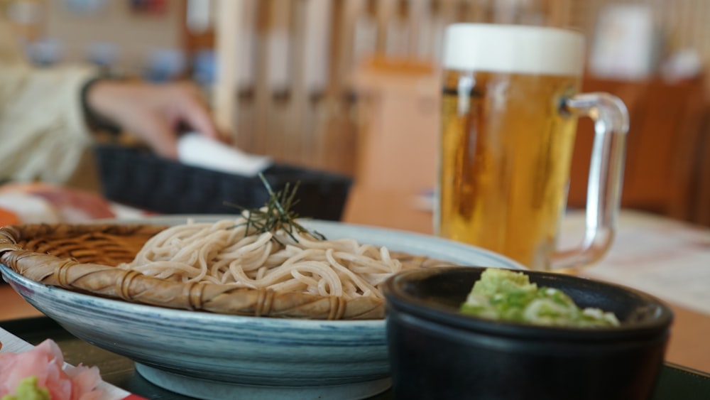 a bowl of noodles and a glass of beer on a table