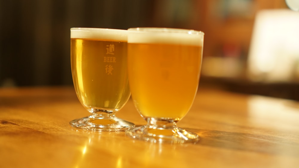 two glasses of beer sitting on top of a wooden table