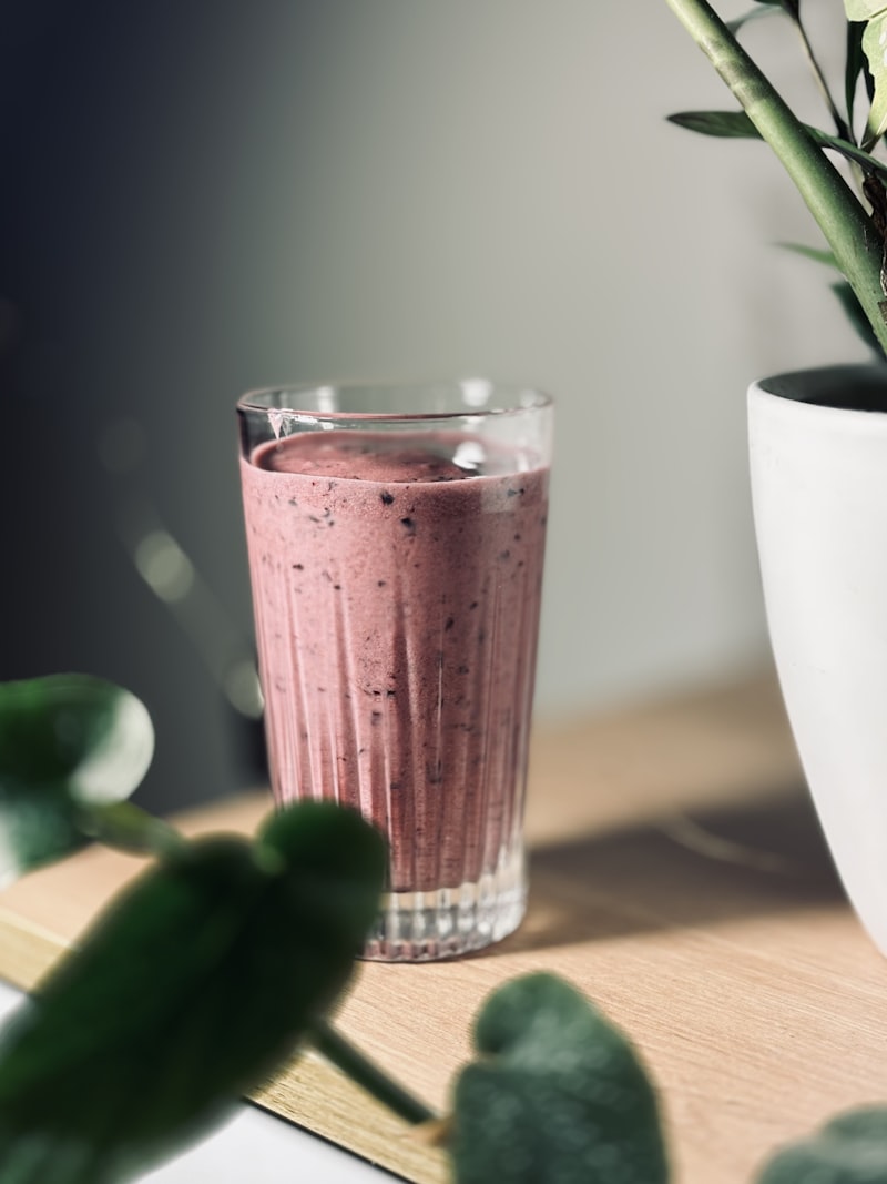 A healthy green smoothie in a glass next to fresh ingredients and a potted plant