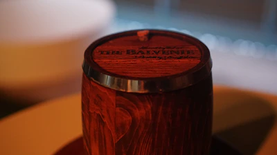 A warm, rustic wooden barrel with the Whiskey Ridge logo etched on it, set against a backdrop of rolling hills.