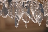 Close-up of ornate crystal glass pieces with intricate, jagged edges, reflecting ambient light. The crystals hang loosely, creating an intricate pattern of light and shadow.
