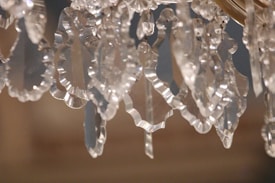 Close-up of ornate crystal glass pieces with intricate, jagged edges, reflecting ambient light. The crystals hang loosely, creating an intricate pattern of light and shadow.