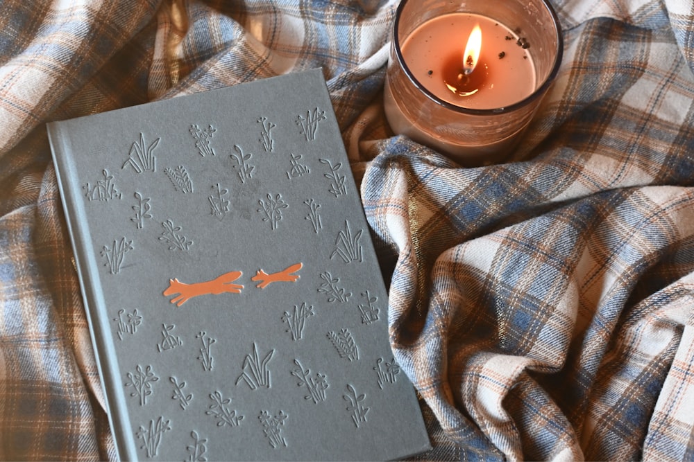 a book sitting on top of a blanket next to a candle