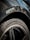 Close-up of a car tire with the brand 'Michelin' and model 'Pilot Sport' clearly visible on the rubber. The rim is sleek and shiny, surrounded by a metallic car body that has some visible water droplets. The background shows a partial reflection on the car's surface.