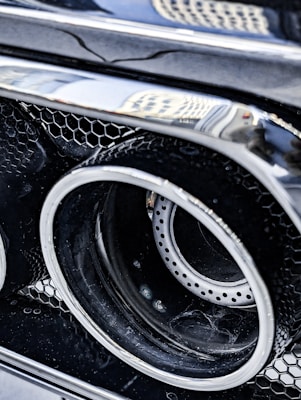 Detailed view of a car's exhaust pipe with a honeycomb-patterned grill. The reflective chrome surface reveals some surrounding environment.