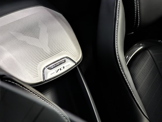 Detail of a car interior featuring a speaker grill with intricate perforated design and 'Corvette 70' branding. The surrounding surfaces include smooth leather with precise stitching.