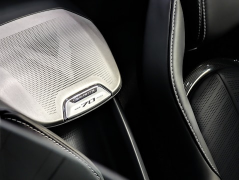 Detail of a car interior featuring a speaker grill with intricate perforated design and 'Corvette 70' branding. The surrounding surfaces include smooth leather with precise stitching.