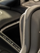 A close-up view of a gray leather car interior, focusing on the stitching detail and texture of the material. The background is slightly blurred, showing parts of the dashboard and console.