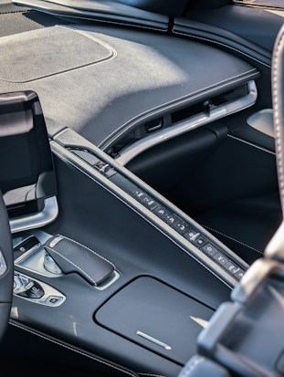 A sleek, modern car interior featuring a central console with buttons arranged neatly in a row. The materials used appear to be high-quality leather and metal, with visible stitching. The design is ergonomic with a gear shift and additional controls nearby.