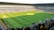 A large soccer stadium filled with a cheering crowd. The field is well-maintained with vibrant green grass, and players can be seen scattered on the pitch. The atmosphere is lively and bustling, typical of a sports event.