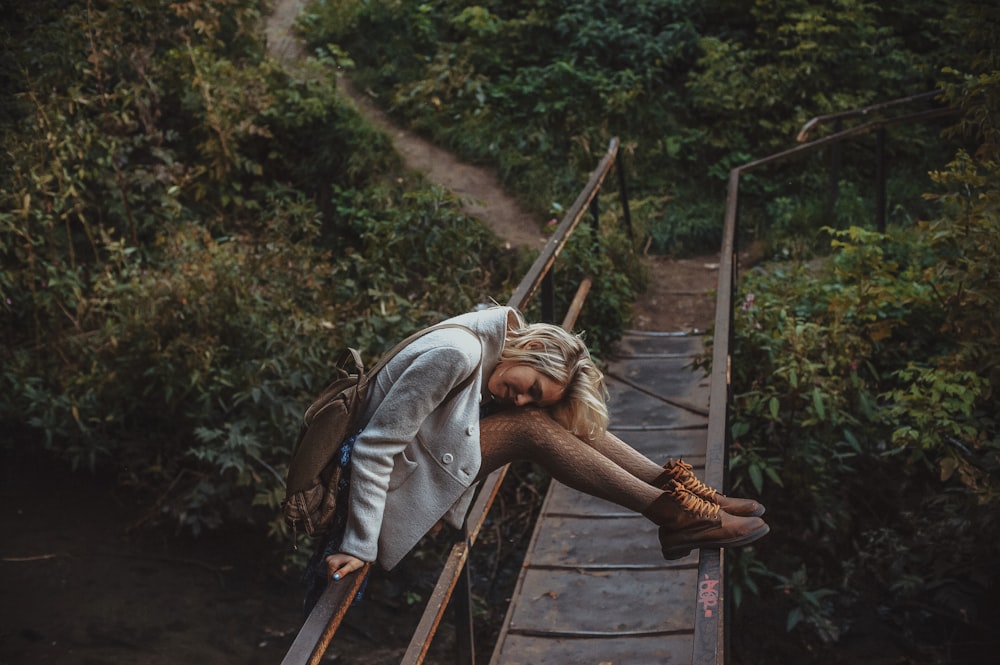 a woman leaning on a wooden bridge in the woods