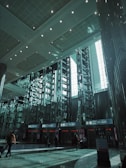 A spacious modern airport terminal features high ceilings and geometric designs. Rows of tall metallic structures and reflective surfaces dominate the scene, while natural light filters through large windows. People with luggage move toward the gates labeled A1-A24.