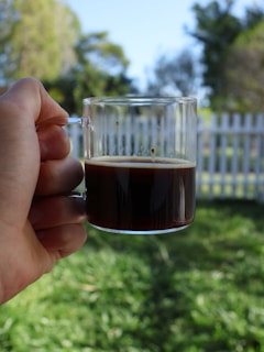 A cheerful parent cheering from the sidelines at a youth soccer game, holding a cup of coffee.