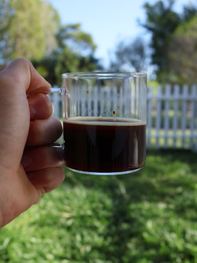 A cheerful parent cheering from the sidelines at a youth soccer game, holding a cup of coffee.