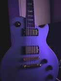 Close-up of a glowing purple guitar neck with skull motifs in a dark setting.