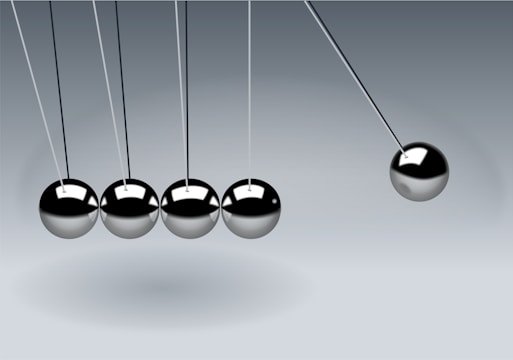 Five metallic spheres are suspended from a frame in a row on thin strings. Four of the spheres are still and touching, while the fifth sphere on the right is pulled away to the side, creating the motion of a Newton's cradle.