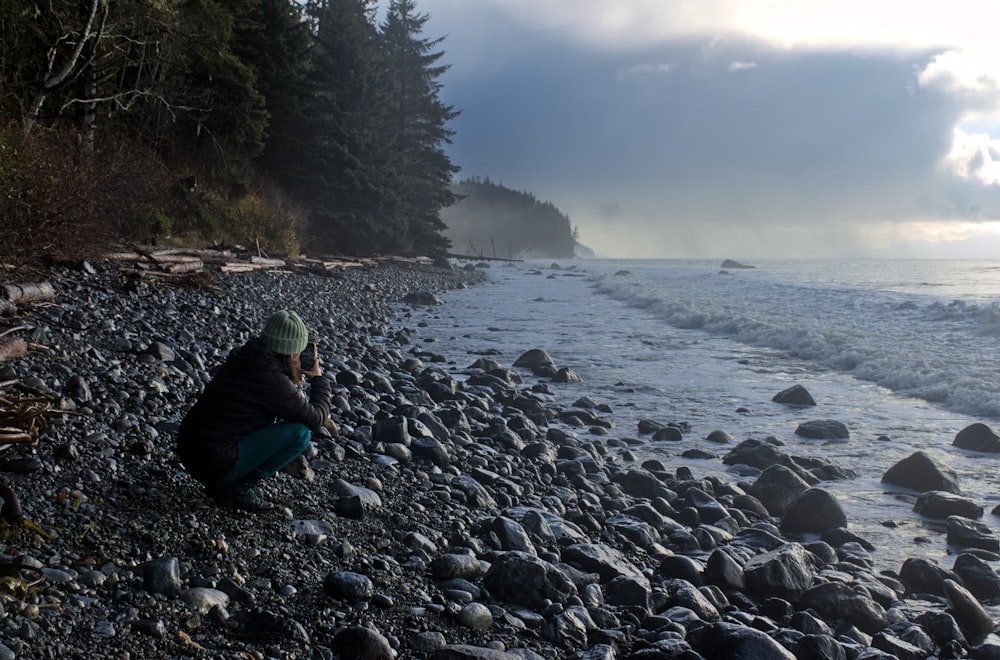 a person sitting on a rocky beach next to the ocean