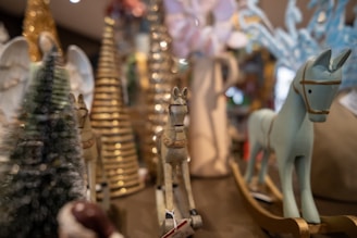 A selection of decorative items including wooden horse figurines, gold cone-shaped objects resembling Christmas trees, and blurred background elements. The arrangement appears to be festive, possibly set for a holiday display.