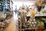 A festive store display featuring a Santa Claus figure on a cart, surrounded by various holiday decorations including silver ornaments, dried floral arrangements, and an assortment of Christmas-themed decor.