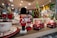 Two toy soldiers stand on a shelf alongside decorative red cars and festive dishware. In the background, a green and red Christmas tree decoration is visible, enhancing the holiday theme. The scene is set in a warmly lit store with an array of holiday ornaments and decorations.
