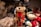A collection of plush teddy bears with one prominently dressed as a soldier in red and gold uniform, complete with a tall black hat and holding a small axe. The surrounding bears are adorned in various outfits, with one holding a red heart. Soft textures and intricate details are visible, creating a festive and cozy atmosphere.