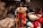 A collection of plush teddy bears with one prominently dressed as a soldier in red and gold uniform, complete with a tall black hat and holding a small axe. The surrounding bears are adorned in various outfits, with one holding a red heart. Soft textures and intricate details are visible, creating a festive and cozy atmosphere.
