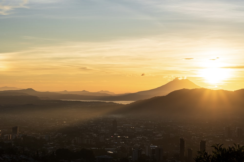 the sun is setting over a city with mountains in the background