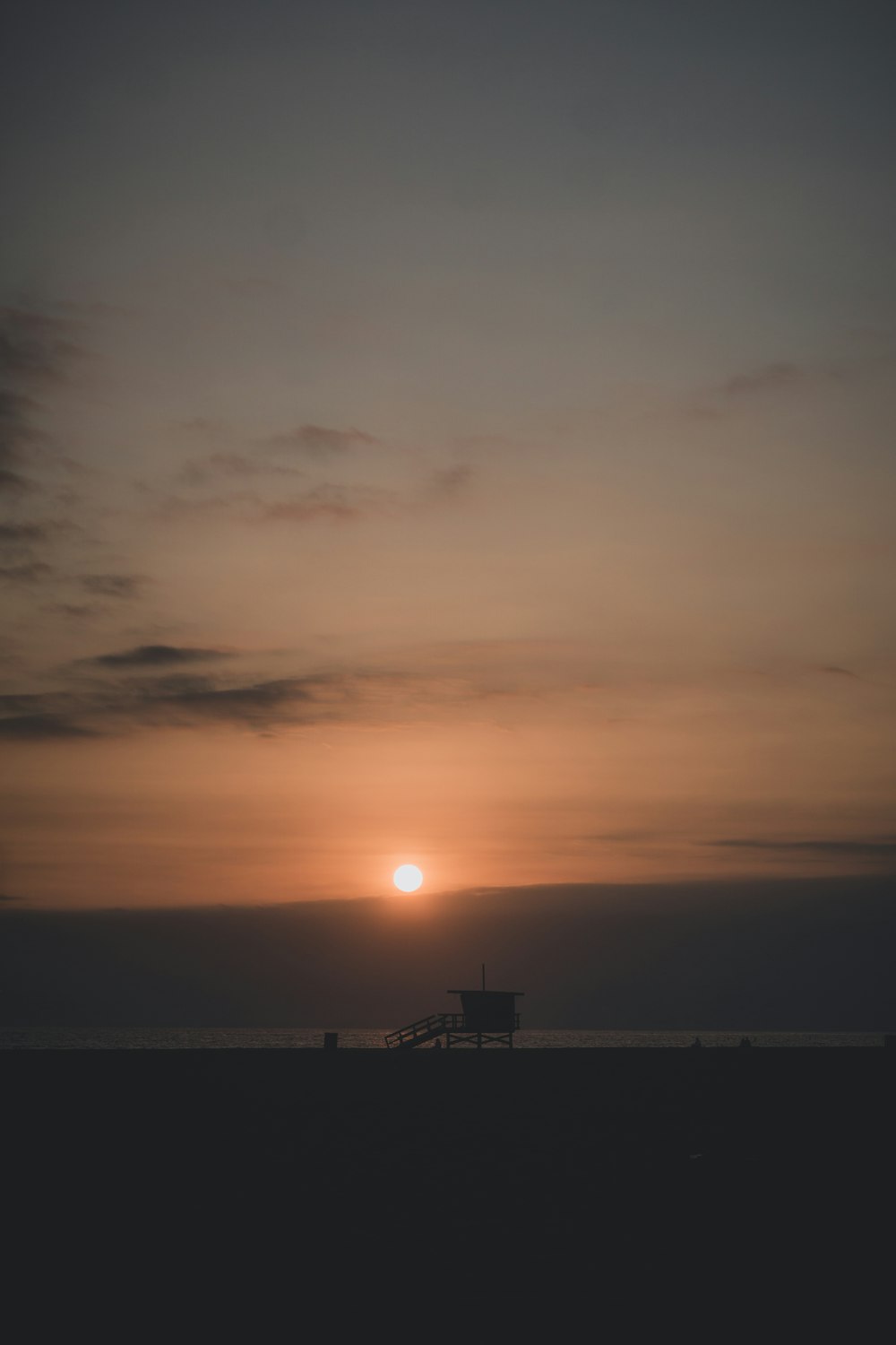 手前にベンチがあり、海に沈む夕日が描かれています