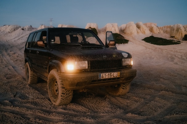 A rugged off-road vehicle covered in light dust, parked on a rocky trail.