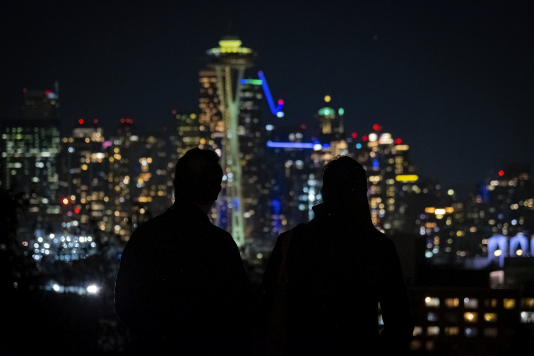a couple of men standing next to each other in front of a city, A silhouette of a couple looking at Seattle Skyline on a