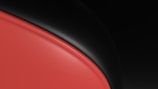 A sleek, glossy design featuring a smooth, curved red surface bordered by a black, voluminous shape. The contrast between the warm red and the cool black creates a modern and abstract aesthetic.