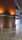 A modern interior space featuring a polished stone floor and wooden walls illuminated by warm, recessed lighting. A grid-like ceiling structure adds architectural interest, and an exterior view of trees is partially visible through glass doors or windows.