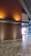 A modern interior space featuring a polished stone floor and wooden walls illuminated by warm, recessed lighting. A grid-like ceiling structure adds architectural interest, and an exterior view of trees is partially visible through glass doors or windows.