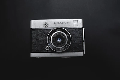 Close-up of a vintage film camera with gold accents against a dark background with film grain texture.