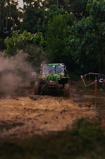 A rugged, off-road vehicle is navigating a muddy terrain surrounded by dense greenery. Dust is kicked up by the tires, creating a dynamic scene of adventure and exploration. The vehicle is prominently marked with decals and appears to be in motion, showcasing its off-road capabilities.