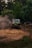 A rugged, off-road vehicle is navigating a muddy terrain surrounded by dense greenery. Dust is kicked up by the tires, creating a dynamic scene of adventure and exploration. The vehicle is prominently marked with decals and appears to be in motion, showcasing its off-road capabilities.