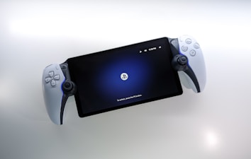 A handheld gaming device is positioned against a white background. The device features a screen displaying a PlayStation logo with the prompt 'To unlock, press the PS button.' It is framed by white controllers on both sides, resembling a hybrid of a tablet and a console.