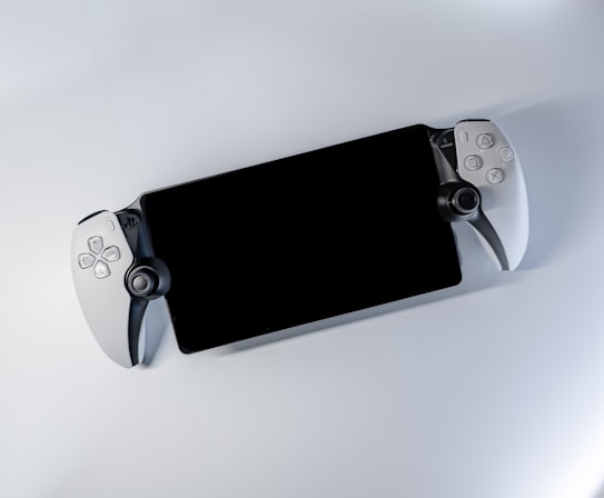 A handheld gaming device with a large screen and game controllers attached on both sides. The controllers have various buttons and joysticks, predominantly in a white and black color scheme, lying on a plain white surface.