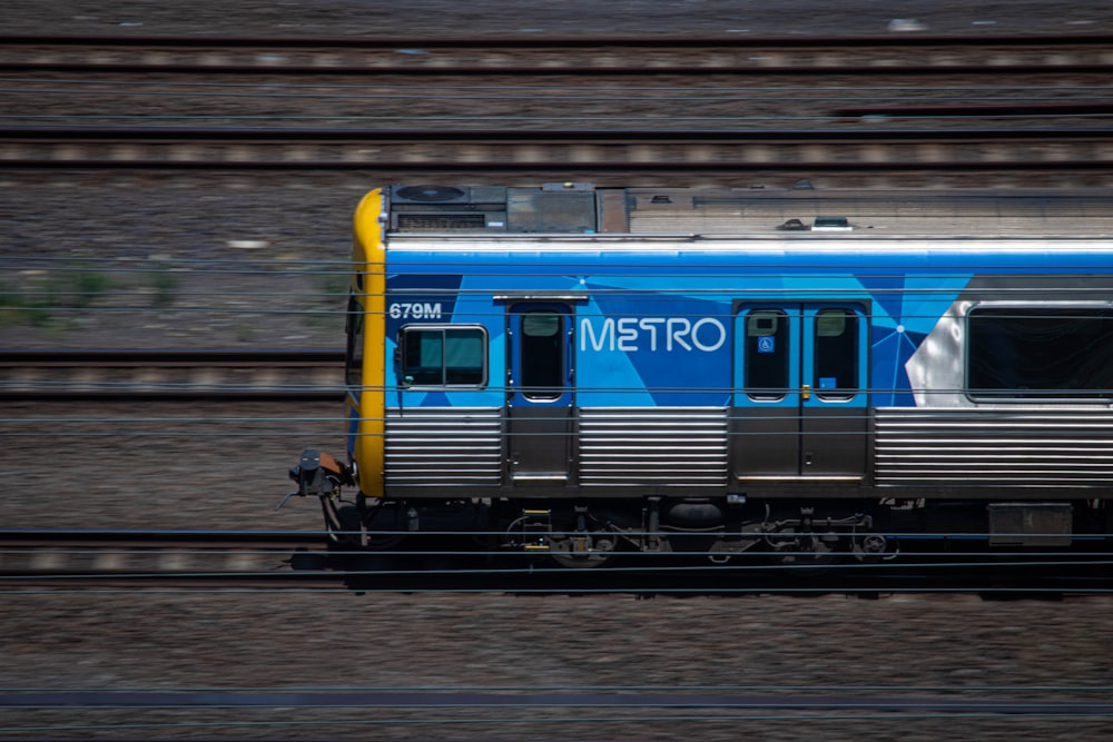 a blue train traveling down train tracks next to a forest