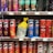 A variety of snack containers are neatly arranged on supermarket shelves. The products include cans of Pringles chips in different flavors such as BBQ, Original, Salt & Vinegar, Habanero, and Scorchin' Sour Cream & Onion. A yellow bag of chips is placed between the cans. Also visible are Doritos Minis Nacho Cheese containers. Prices are displayed on tags below each row.