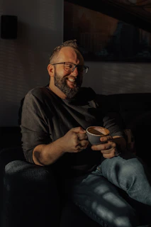 Lifestyle shot of a man enjoying morning coffee, beard perfectly groomed, in a warm neutral-toned setting.