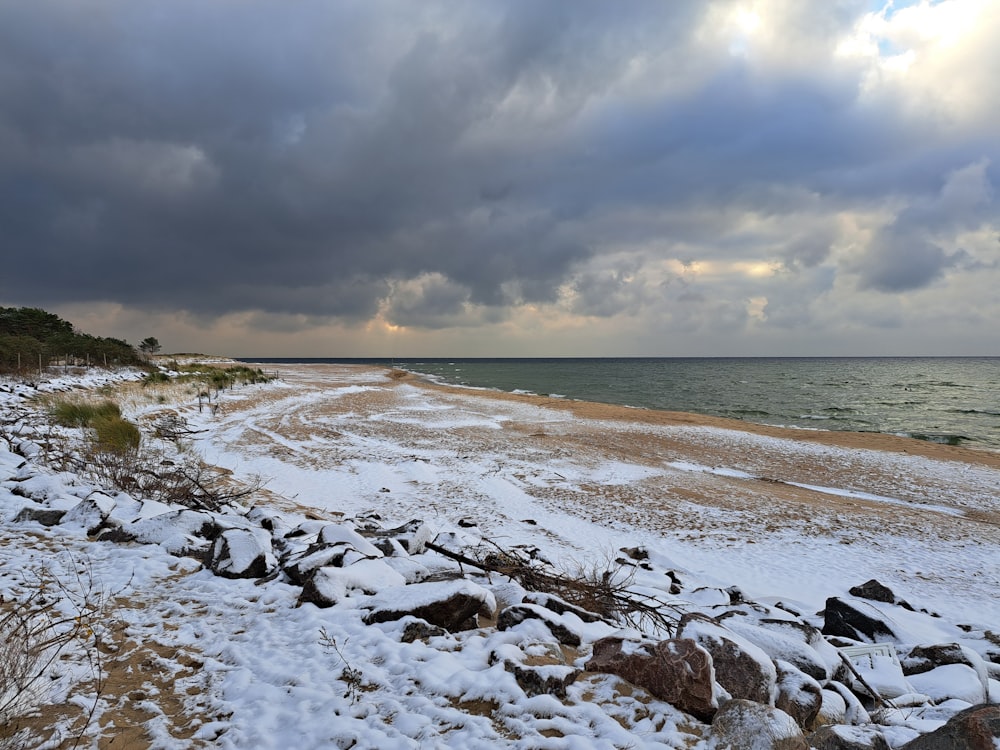 a sandy beach covered in snow under a cloudy sky