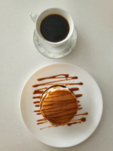 Close-up of a steaming cup of coffee next to a plate of golden pancakes with syrup.