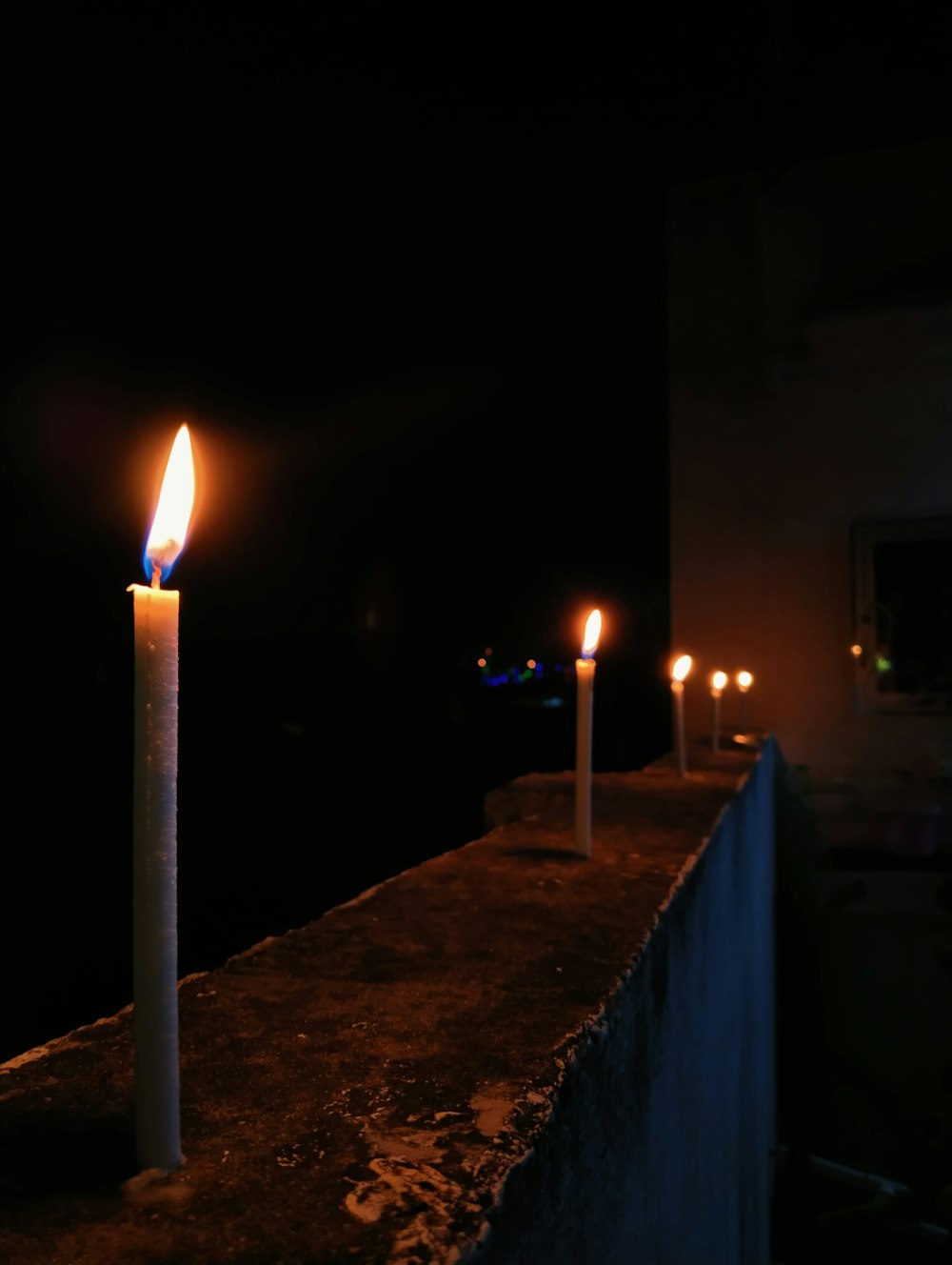 a row of lit candles sitting on top of a cement wall