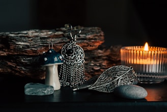 A serene arrangement featuring a small mushroom sculpture, an intricate metallic dreamcatcher, a lit candle in a transparent holder, and smooth stones. The background consists of stacked pieces of wood, adding a rustic feel.