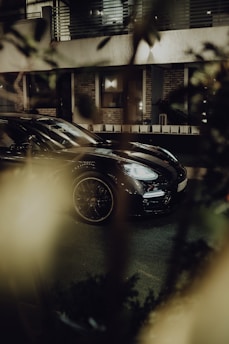 Luxury black car parked in front of an elegant modern building at dusk.