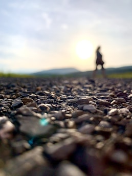 a person standing on a rocky road with the sun in the background